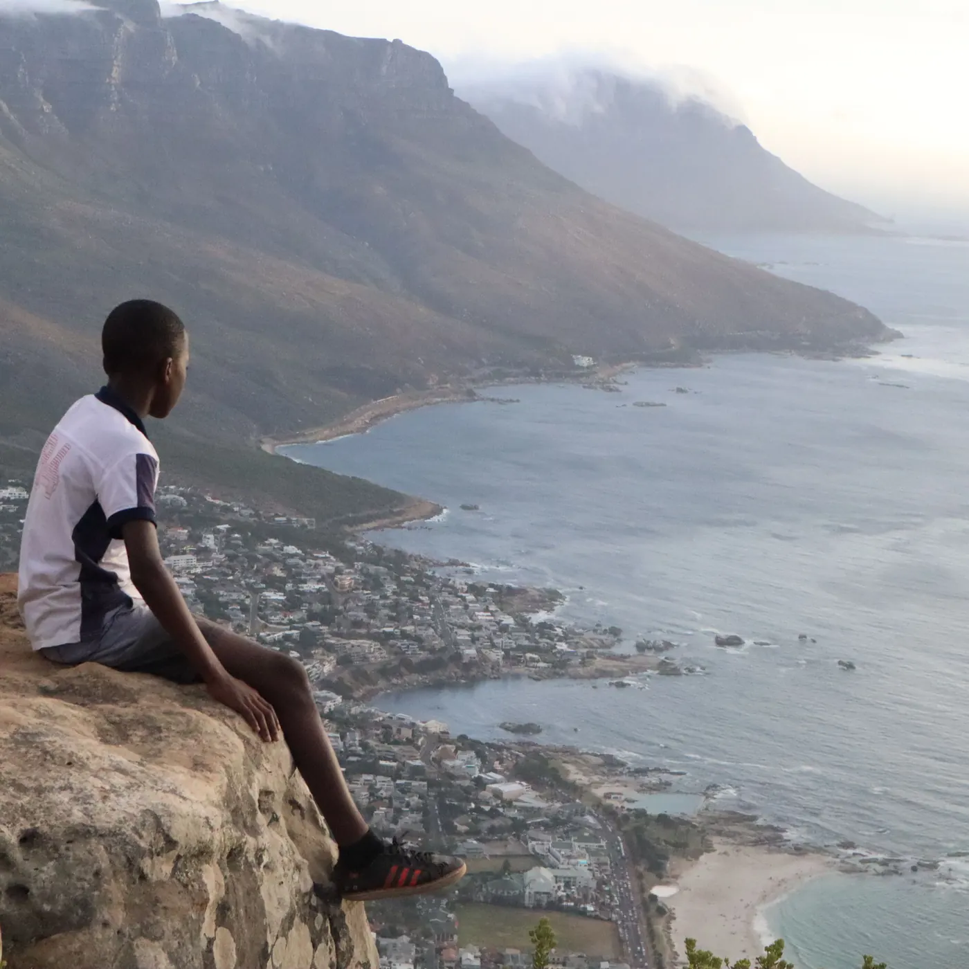 A boy sits on a rock high above Cape Town and looks out over the coast
