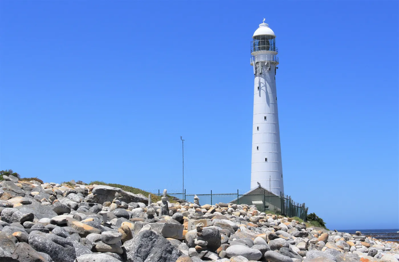 A white lighthouse behind a beach of stacked stones near Cape Town